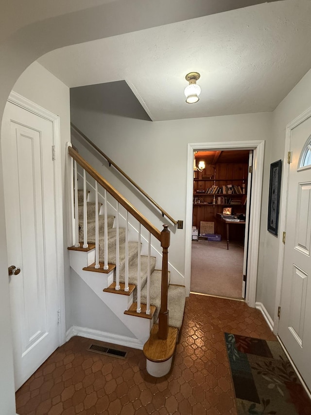 foyer entrance featuring stairway, carpet floors, baseboards, tile patterned flooring, and visible vents