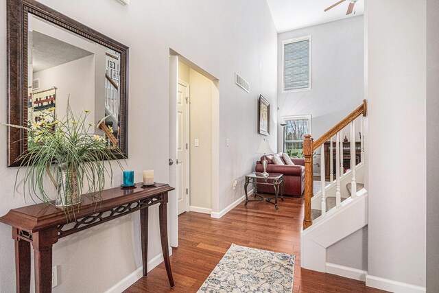 entryway with wood finished floors, stairs, baseboards, a high ceiling, and visible vents