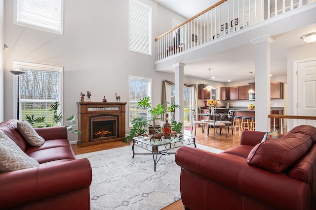 living area with ornate columns, a lit fireplace, a towering ceiling, and light wood-type flooring