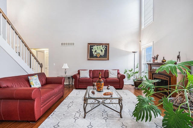 living room with stairway, a high ceiling, wood finished floors, visible vents, and a fireplace