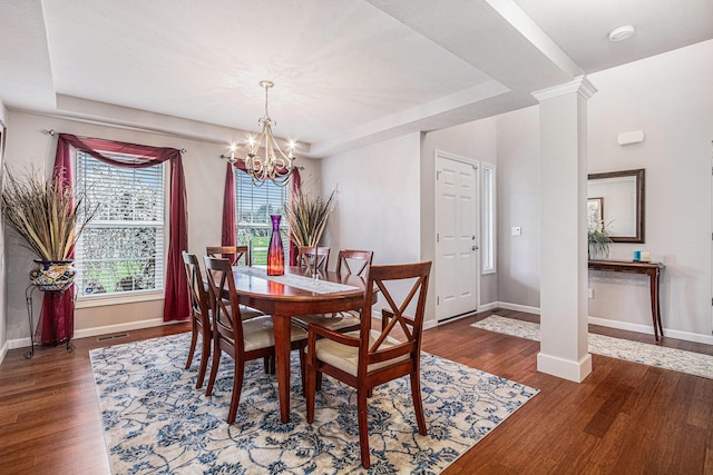 dining room featuring a tray ceiling, decorative columns, baseboards, a notable chandelier, and wood finished floors