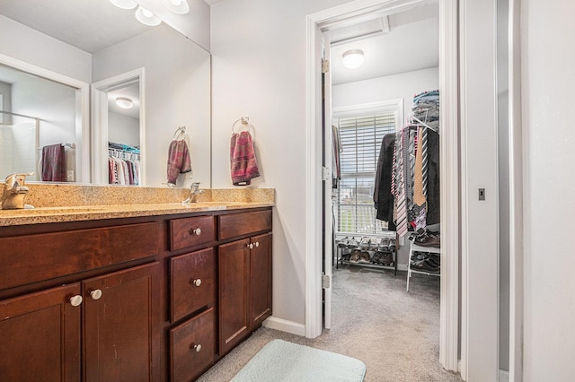 full bathroom featuring double vanity, baseboards, a sink, and a walk in closet