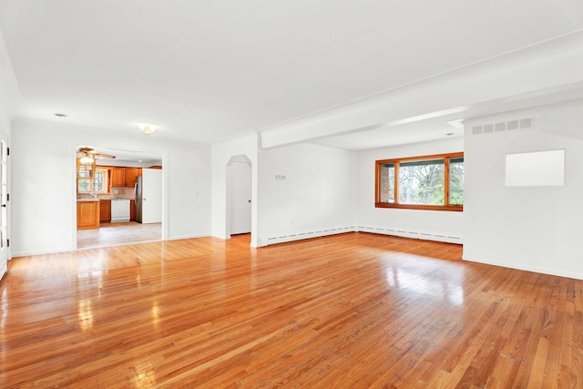 unfurnished living room with light wood-style floors, arched walkways, baseboards, and visible vents