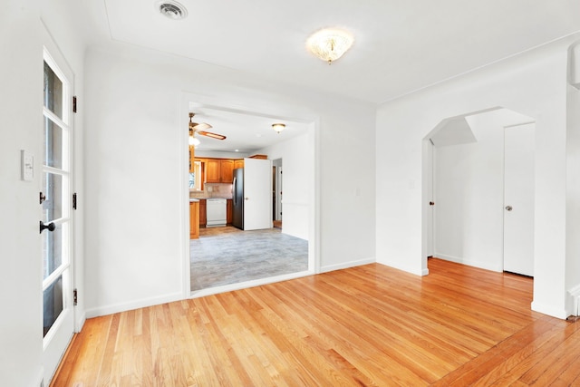 spare room with arched walkways, baseboards, light wood finished floors, and visible vents