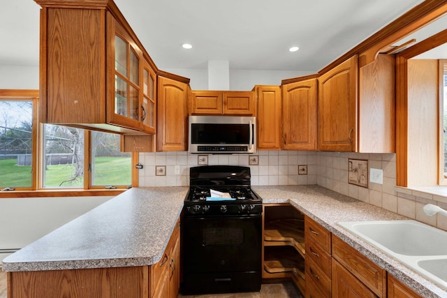 kitchen with black gas range oven, a sink, brown cabinetry, stainless steel microwave, and glass insert cabinets