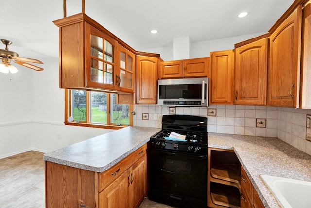 kitchen featuring black gas range oven, a peninsula, stainless steel microwave, backsplash, and glass insert cabinets