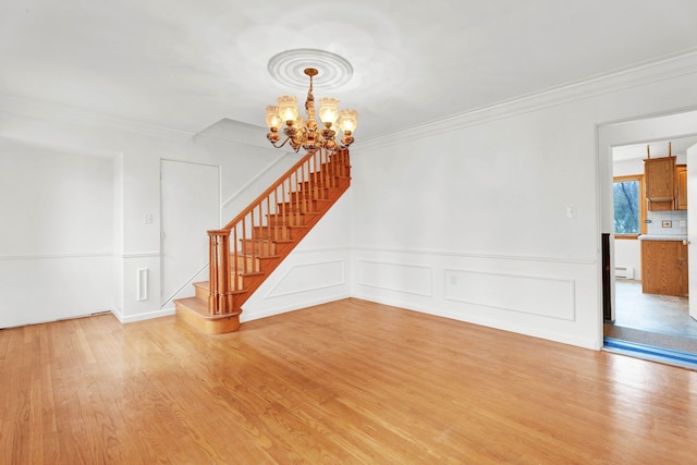 unfurnished living room with wainscoting, stairway, a notable chandelier, ornamental molding, and light wood-style flooring