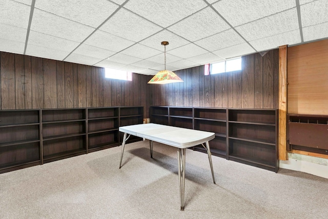 carpeted home office with wood walls and a paneled ceiling