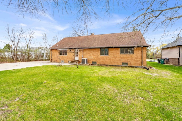 rear view of property featuring central AC unit, a shingled roof, a yard, and brick siding
