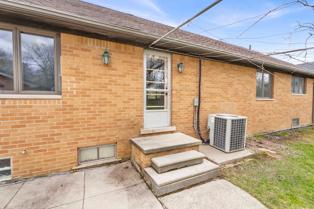 entrance to property featuring central air condition unit, brick siding, and a shingled roof