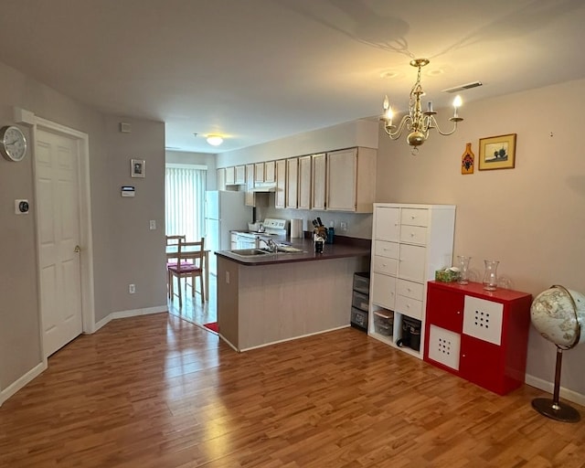 kitchen with dark countertops, wood finished floors, white appliances, baseboards, and a peninsula