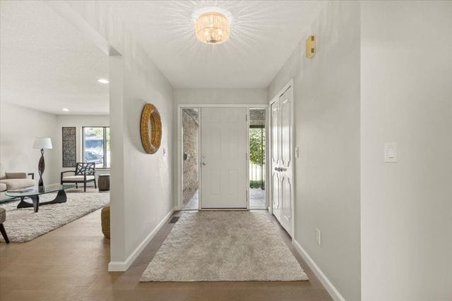 foyer entrance with baseboards, wood finished floors, and a chandelier