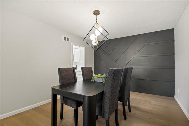 dining area with a decorative wall, light wood-type flooring, visible vents, and baseboards