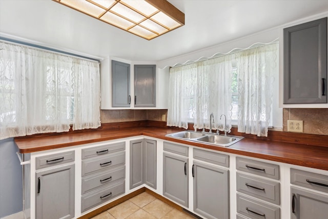 kitchen featuring butcher block countertops, a sink, light tile patterned flooring, and gray cabinets