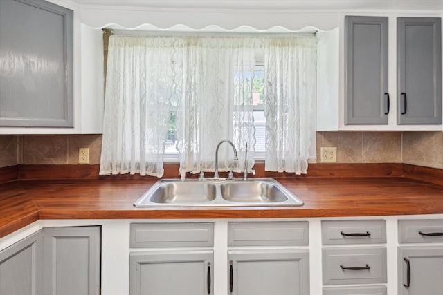 kitchen featuring butcher block counters, a sink, backsplash, and gray cabinets