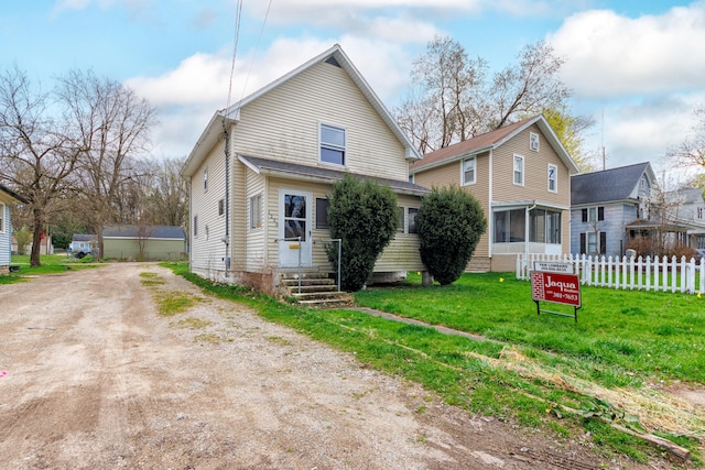 back of house featuring fence, a lawn, and dirt driveway