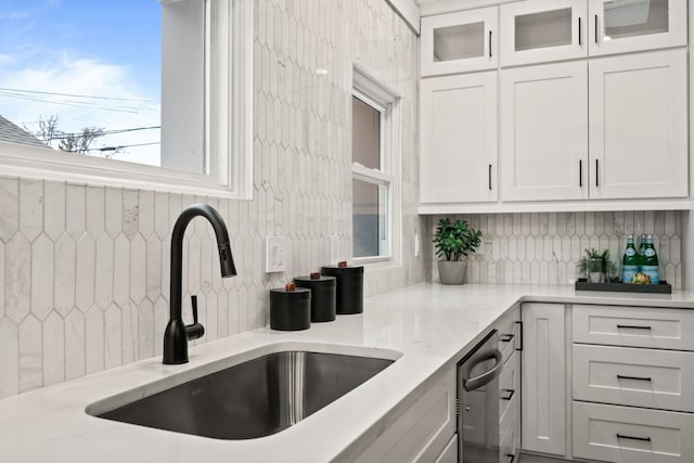 kitchen with tasteful backsplash, white cabinetry, light stone counters, and a sink