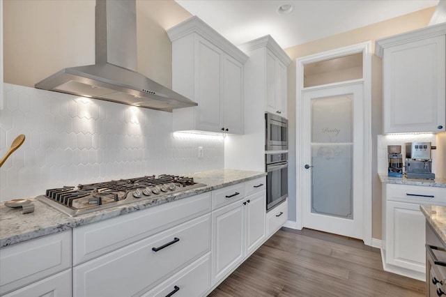 kitchen with wall chimney exhaust hood, white cabinets, dark wood-style flooring, backsplash, and appliances with stainless steel finishes