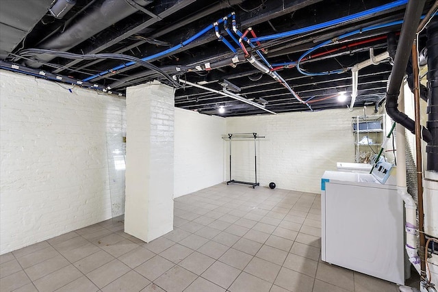 basement featuring brick wall, washing machine and clothes dryer, and tile patterned floors