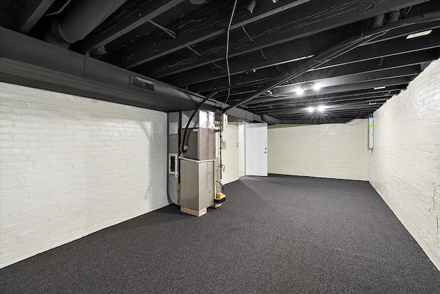 finished basement featuring brick wall, heating unit, and visible vents