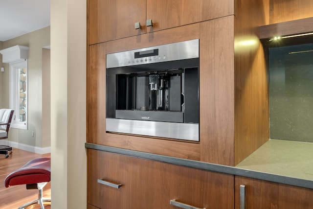 details featuring wood finished floors, stainless steel oven, baseboards, and brown cabinetry