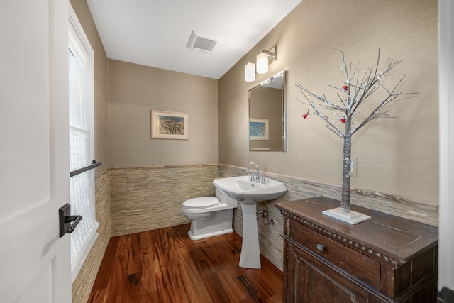 half bathroom with wood finished floors, visible vents, toilet, a sink, and tile walls