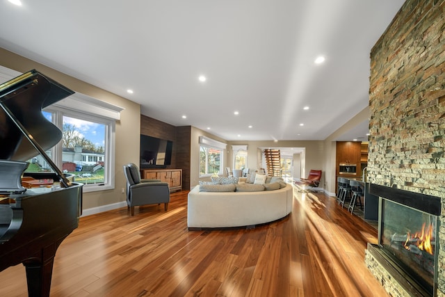 living area with a stone fireplace, a healthy amount of sunlight, wood finished floors, and recessed lighting