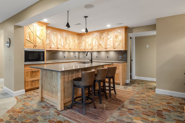 kitchen featuring baseboards, black microwave, a sink, and stone flooring