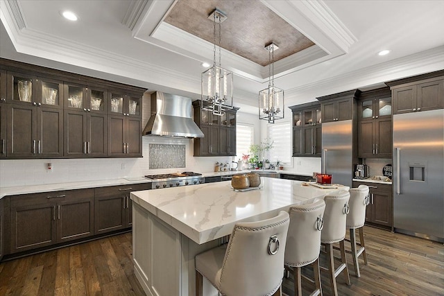 3888 Thatcher Dr, Rochester Hills, MI 48309 - kitchen featuring stainless steel appliances, a center island, a tray ceiling, dark wood finished floors, and wall chimney range hood