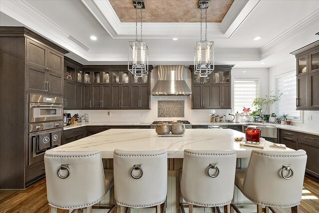3888 Thatcher Dr, Rochester Hills, MI 48309 - kitchen with wall chimney exhaust hood, dark brown cabinetry, a tray ceiling, and a kitchen island