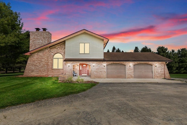 view of front of property featuring a front lawn, a chimney, brick siding, an attached garage, and driveway