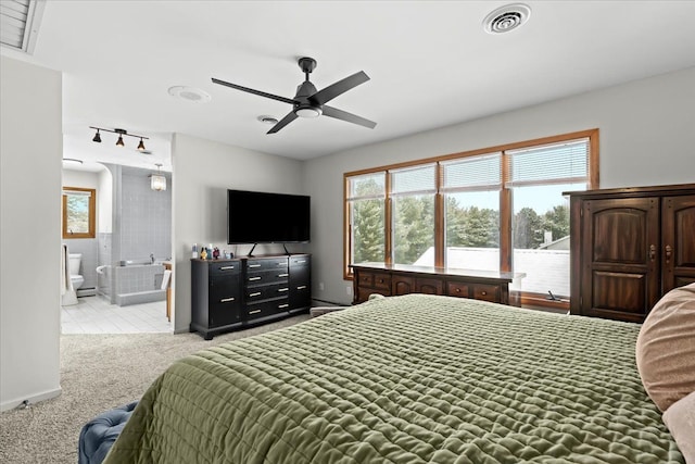 bedroom featuring visible vents, rail lighting, baseboards, ensuite bathroom, and light carpet
