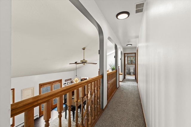 corridor with arched walkways, visible vents, dark carpet, and a baseboard heating unit