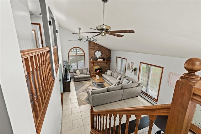 living area with a ceiling fan, vaulted ceiling, light tile patterned floors, and a fireplace