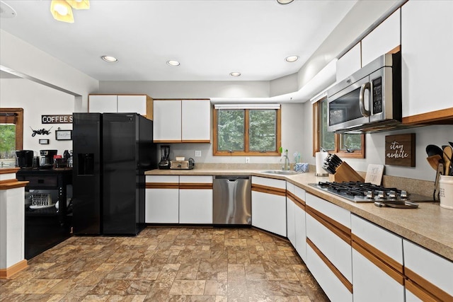 kitchen featuring a healthy amount of sunlight, stone finish floor, white cabinetry, a sink, and stainless steel appliances