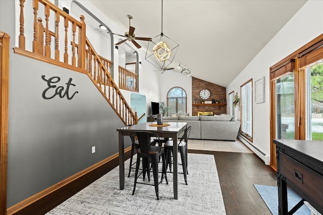 dining area featuring baseboard heating, wood finished floors, stairway, high vaulted ceiling, and ceiling fan with notable chandelier
