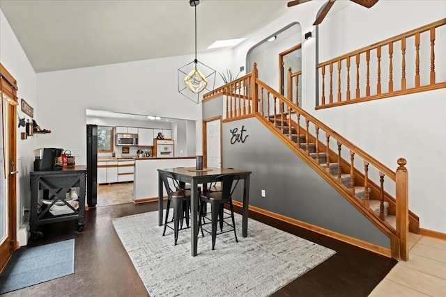 dining area with a ceiling fan, wood finished floors, high vaulted ceiling, baseboards, and stairs