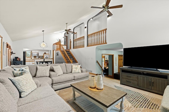 living area with stairway, ceiling fan, light tile patterned floors, and high vaulted ceiling