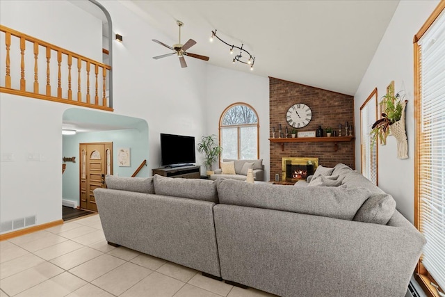 living area with light tile patterned flooring, ceiling fan, a fireplace, high vaulted ceiling, and visible vents