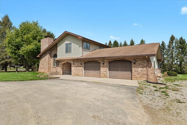 traditional-style home with driveway, a chimney, a front yard, a garage, and brick siding