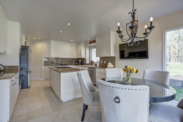 kitchen with an inviting chandelier, a center island, white cabinets, tasteful backsplash, and stainless steel appliances