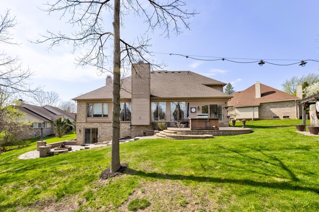back of property with a chimney, a patio area, an outdoor fire pit, a yard, and a jacuzzi