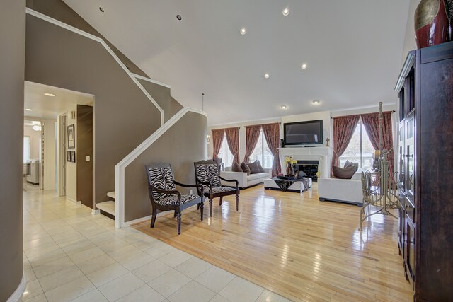 living room featuring light tile patterned flooring, high vaulted ceiling, a glass covered fireplace, stairs, and baseboards
