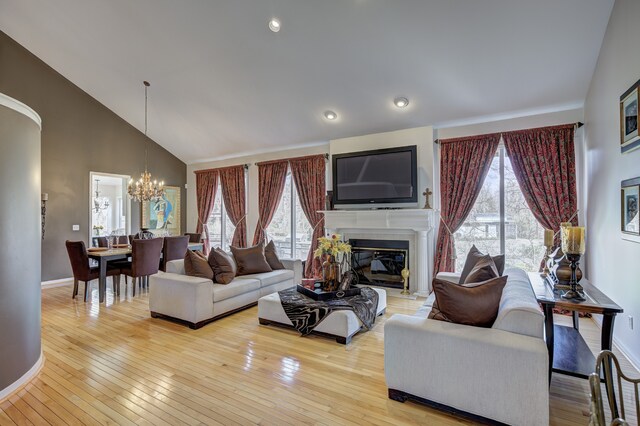 living area featuring a glass covered fireplace, high vaulted ceiling, wood-type flooring, and a notable chandelier