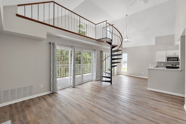 unfurnished living room featuring high vaulted ceiling, stairs, light wood-style floors, baseboards, and visible vents