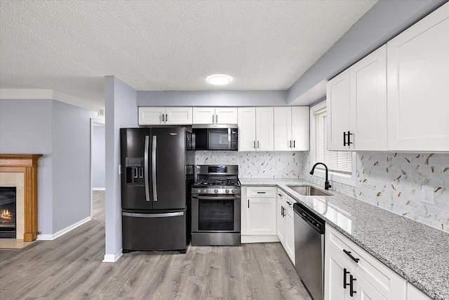 kitchen with light stone counters, appliances with stainless steel finishes, a sink, and light wood-style flooring