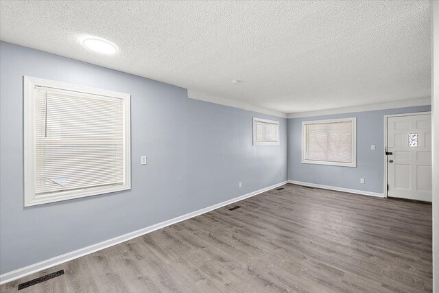 interior space featuring baseboards, wood finished floors, a textured ceiling, and visible vents