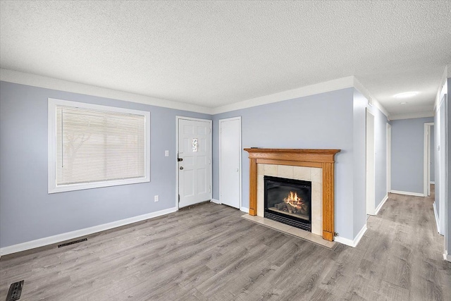 unfurnished living room featuring a textured ceiling, a tile fireplace, visible vents, and wood finished floors