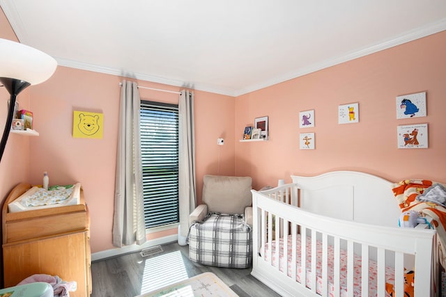 bedroom with baseboards, crown molding, wood finished floors, and a crib