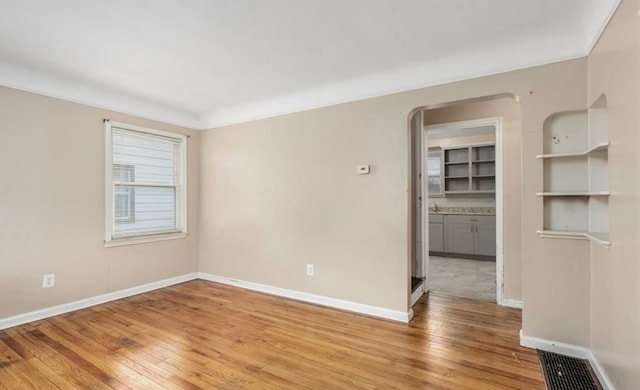 unfurnished room featuring light wood-style flooring, arched walkways, and baseboards